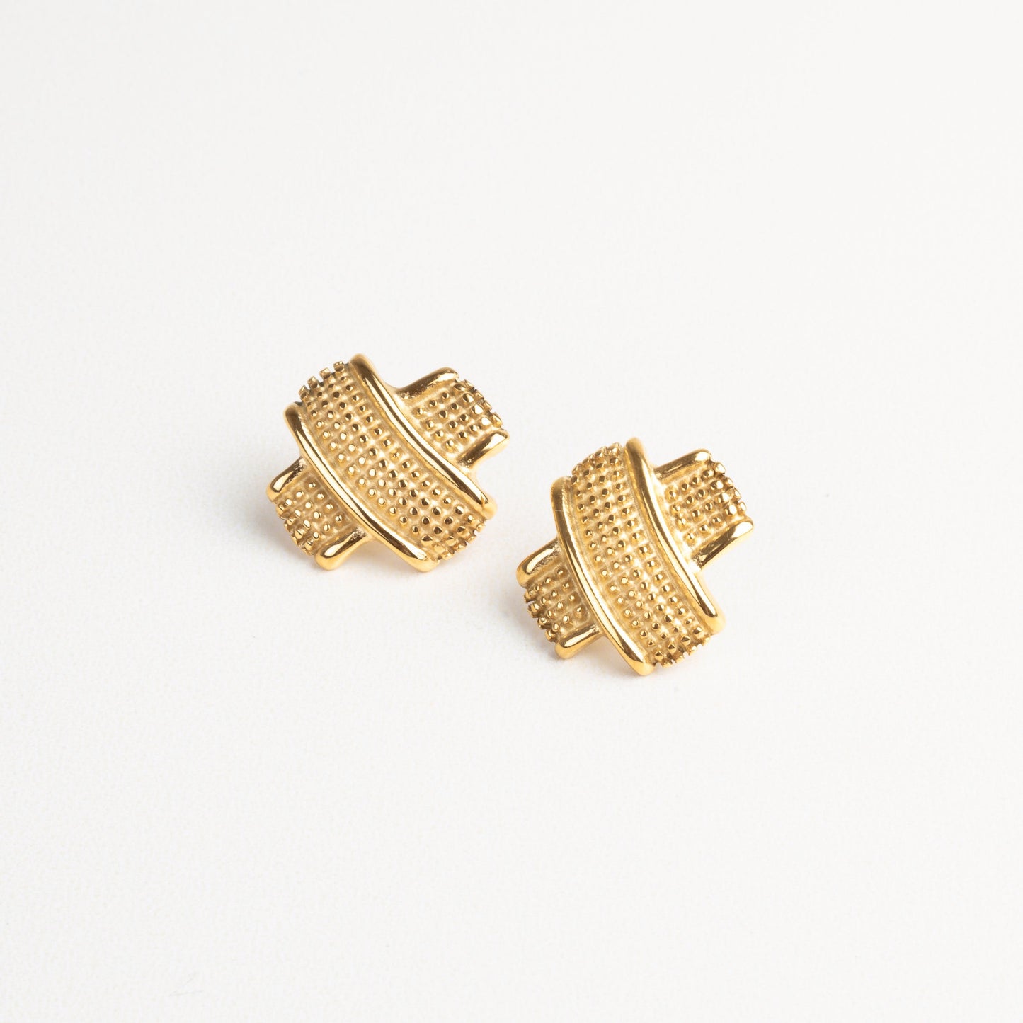 Vista frontal de aretes tipo tacha dorados con textura, diseño moderno y elegante.