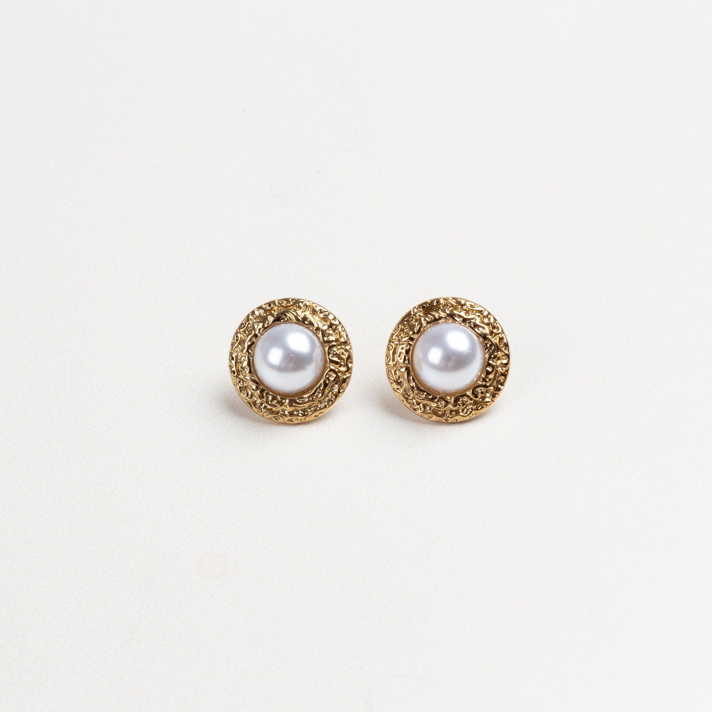 Aretes redondos con borde dorado texturizado y una perla en el centro, que combinan elegancia clásica con un diseño moderno y detallado, ideales para elevar cualquier atuendo con un toque sofisticado.