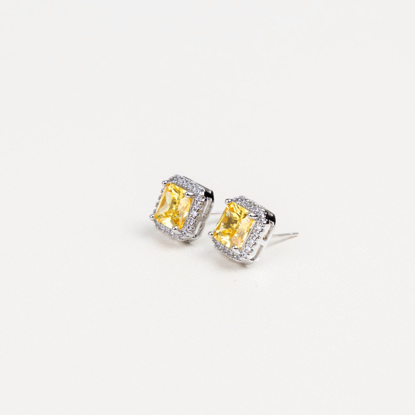 Detalle de la estructura cuadrada de los aretes, con el resplandor dorado de las zirconias amarillas reflejando la luz de manera deslumbrante.