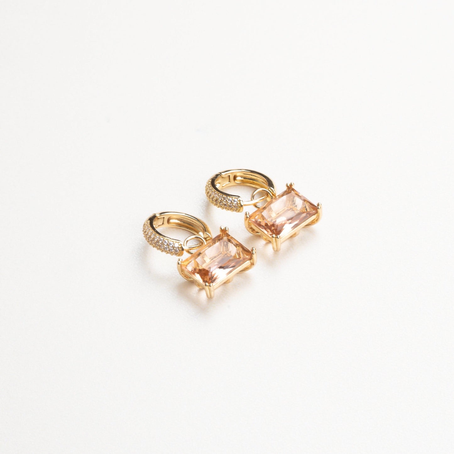 Primer plano de los aretes arracadas con zirconia cuadrada colgando, donde se puede apreciar el destello de la piedra y el diseño limpio y moderno de la joya.