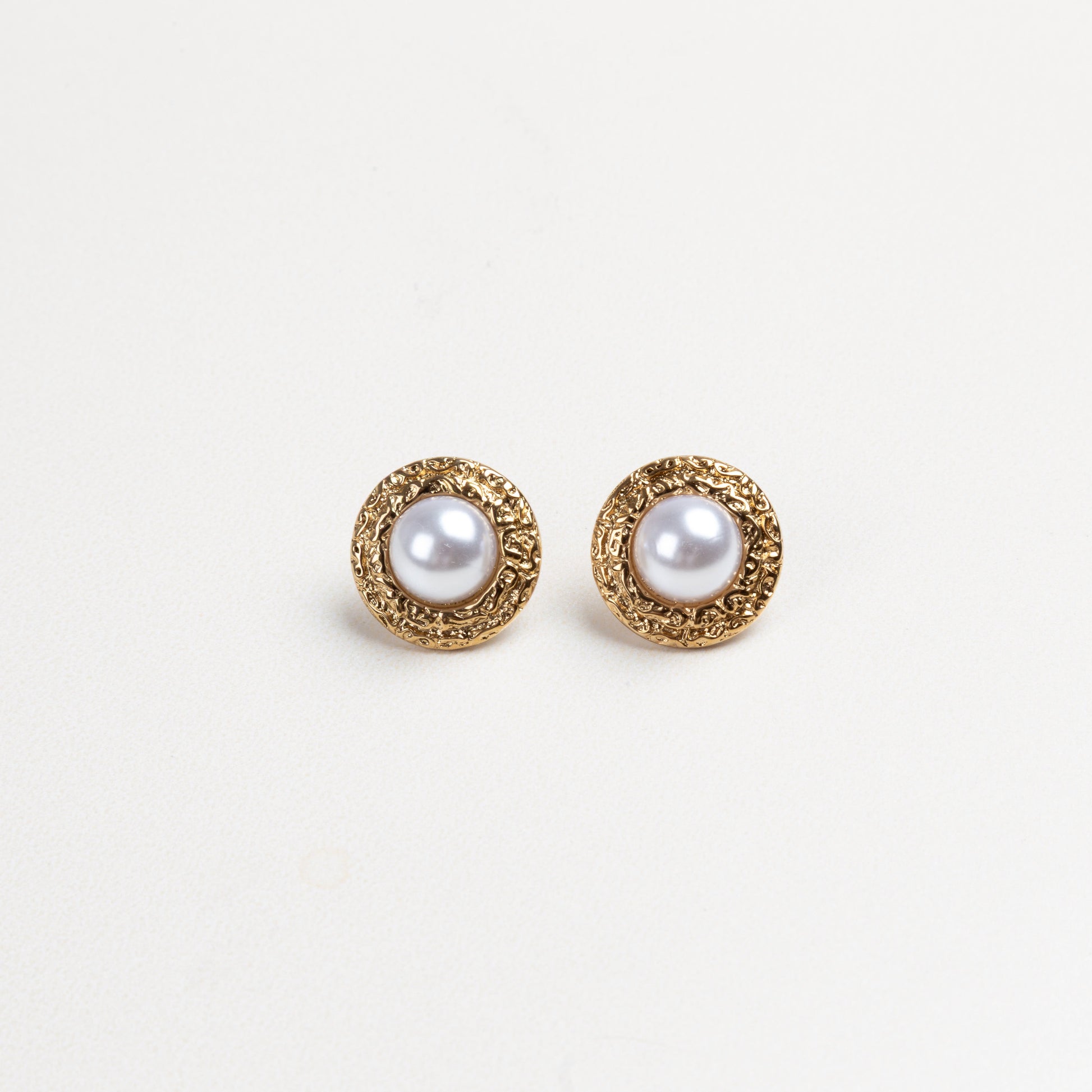 Aretes redondos con borde dorado texturizado y una perla en el centro, que combinan elegancia clásica con un diseño moderno y detallado, ideales para elevar cualquier atuendo con un toque sofisticado.
